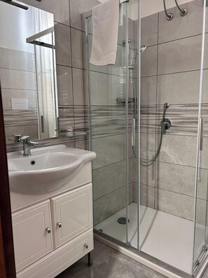 A modern bathroom with a glass-enclosed shower, a white sink, and a vanity with drawers. - B&B Metropolitan RC (Reggio Calabria)