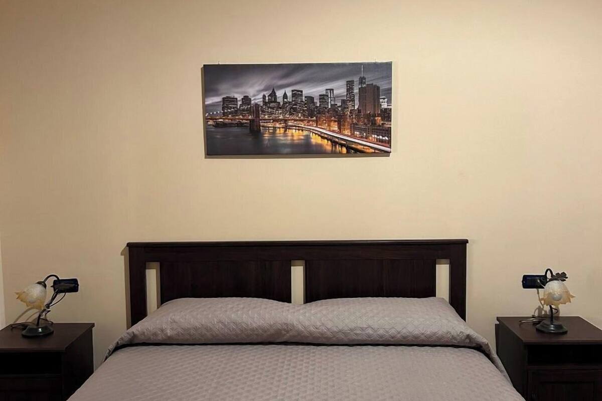 A hotel room with a bed, two nightstands, a cityscape painting on the wall, and two towels on the bed.