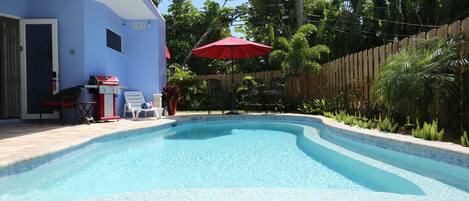A swimming pool with a wooden deck, a barbecue grill, and a red umbrella.