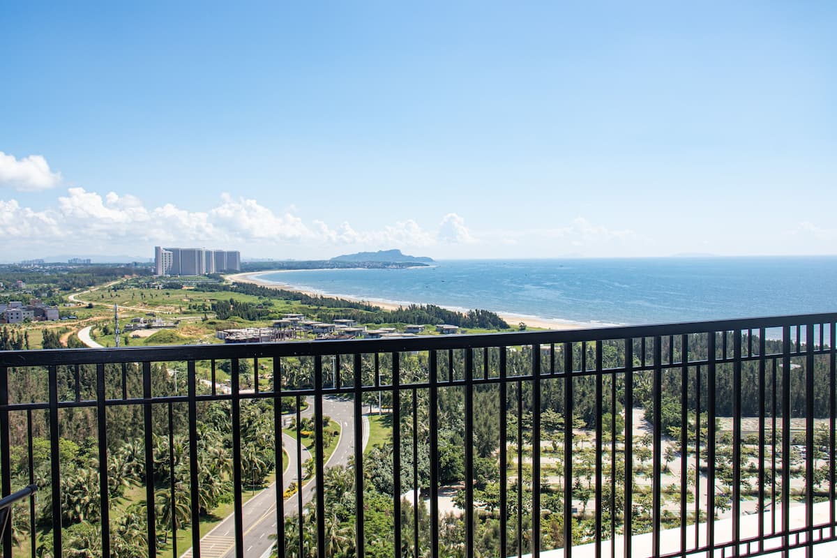 A coastal view from a balcony with a clear sky, a beach, and a distant mountain.