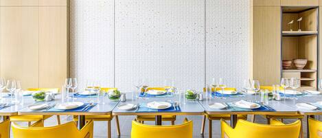 A dining area with a long table set for multiple people, yellow chairs, and a patterned wall in the background.
