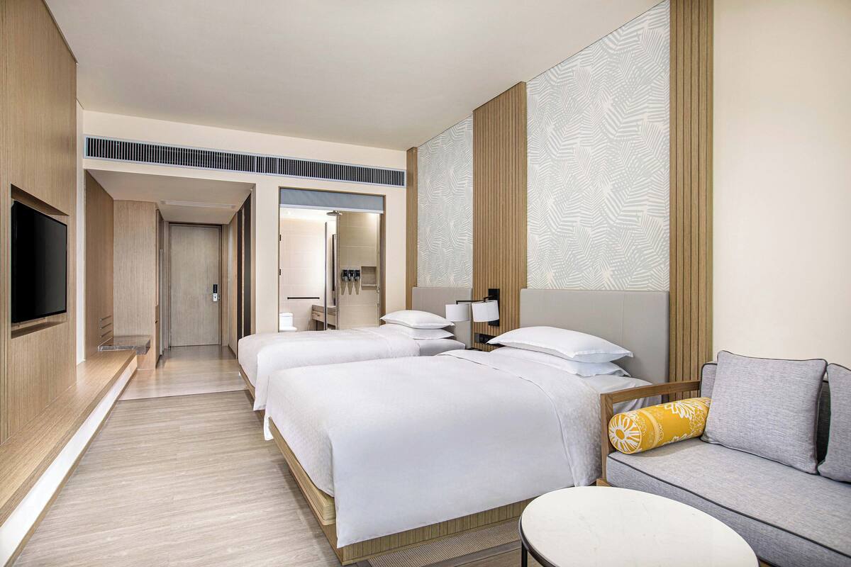 A hotel room with two beds, a sofa, a TV, and a bathroom visible through an open door.