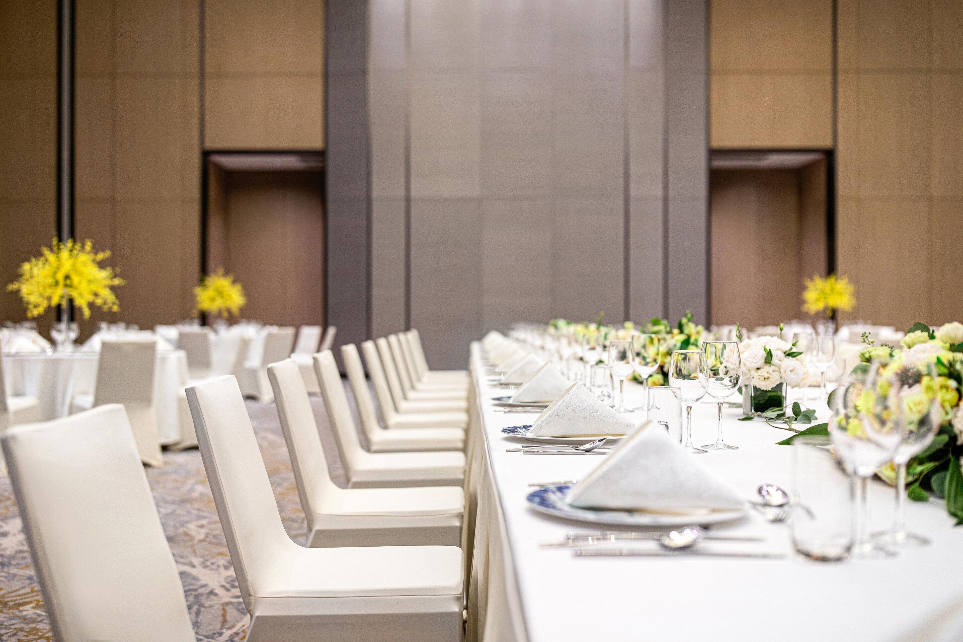 Une longue table de banquet, agrémentée de chaises blanches, de compositions florales et d’une décoration de table élégante.