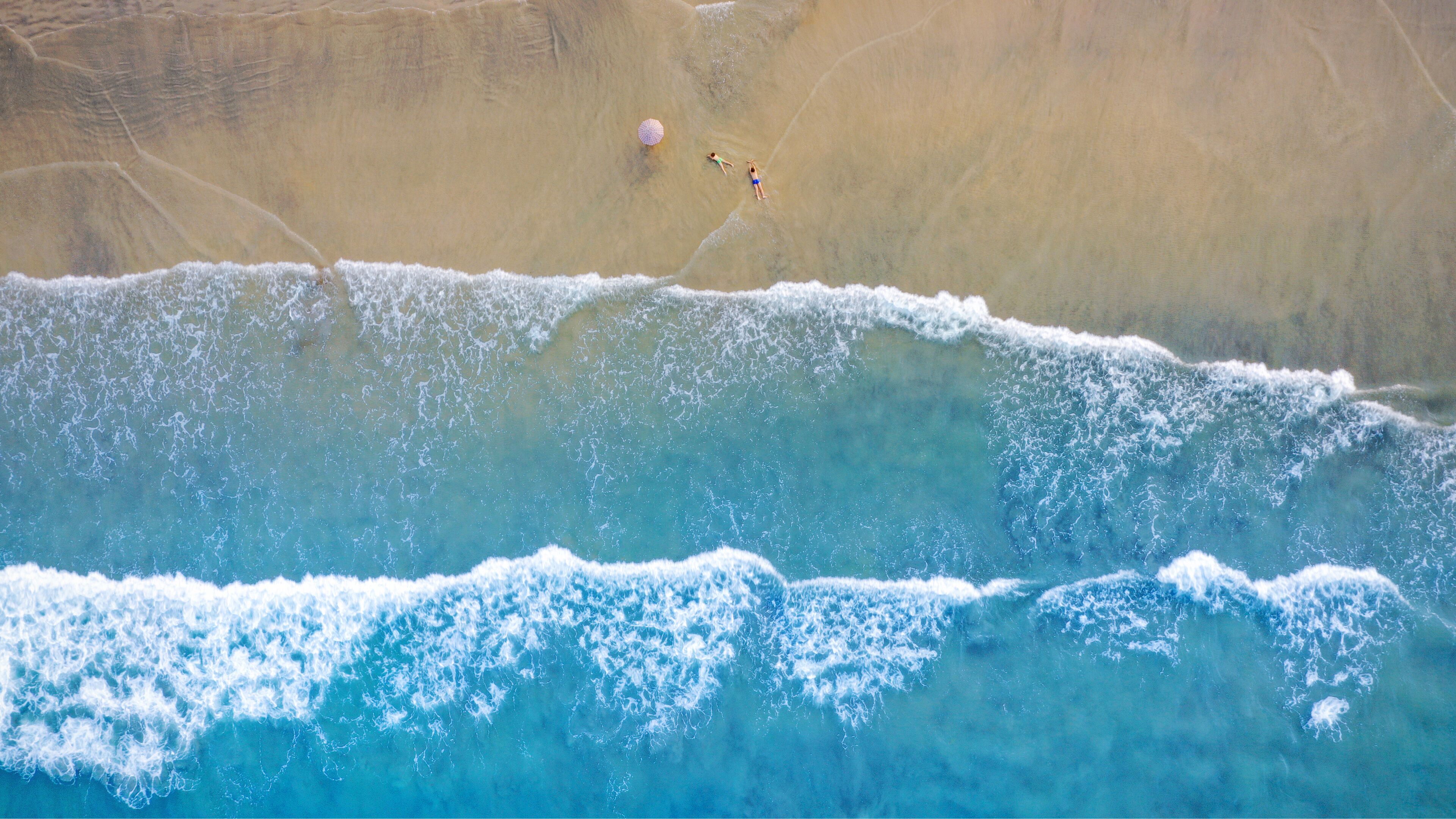 Vista aérea de una playa con dos personas y una sombrilla.