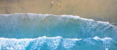 Vista aérea de una playa con dos personas y una sombrilla.