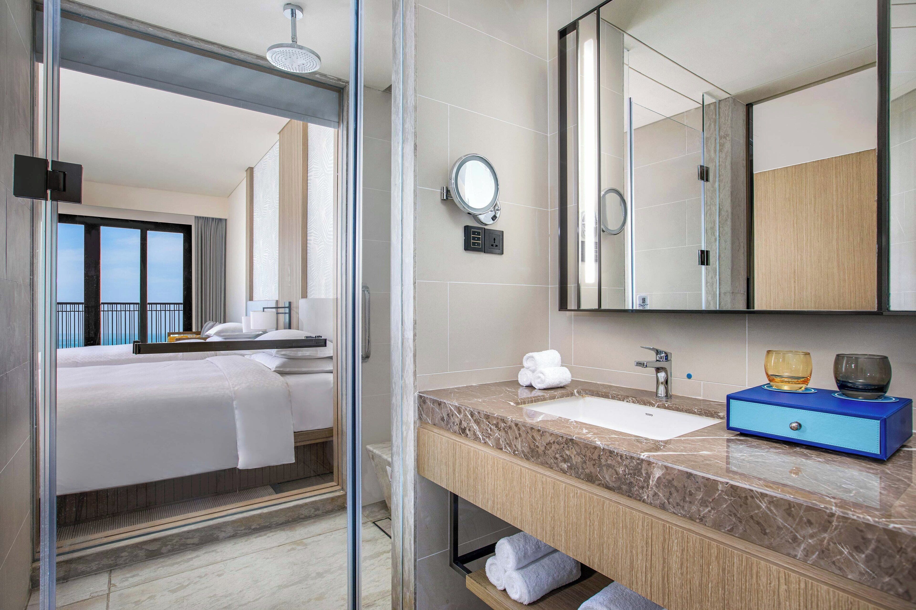 A modern hotel bathroom with a large mirror, a sink, and a shower area.