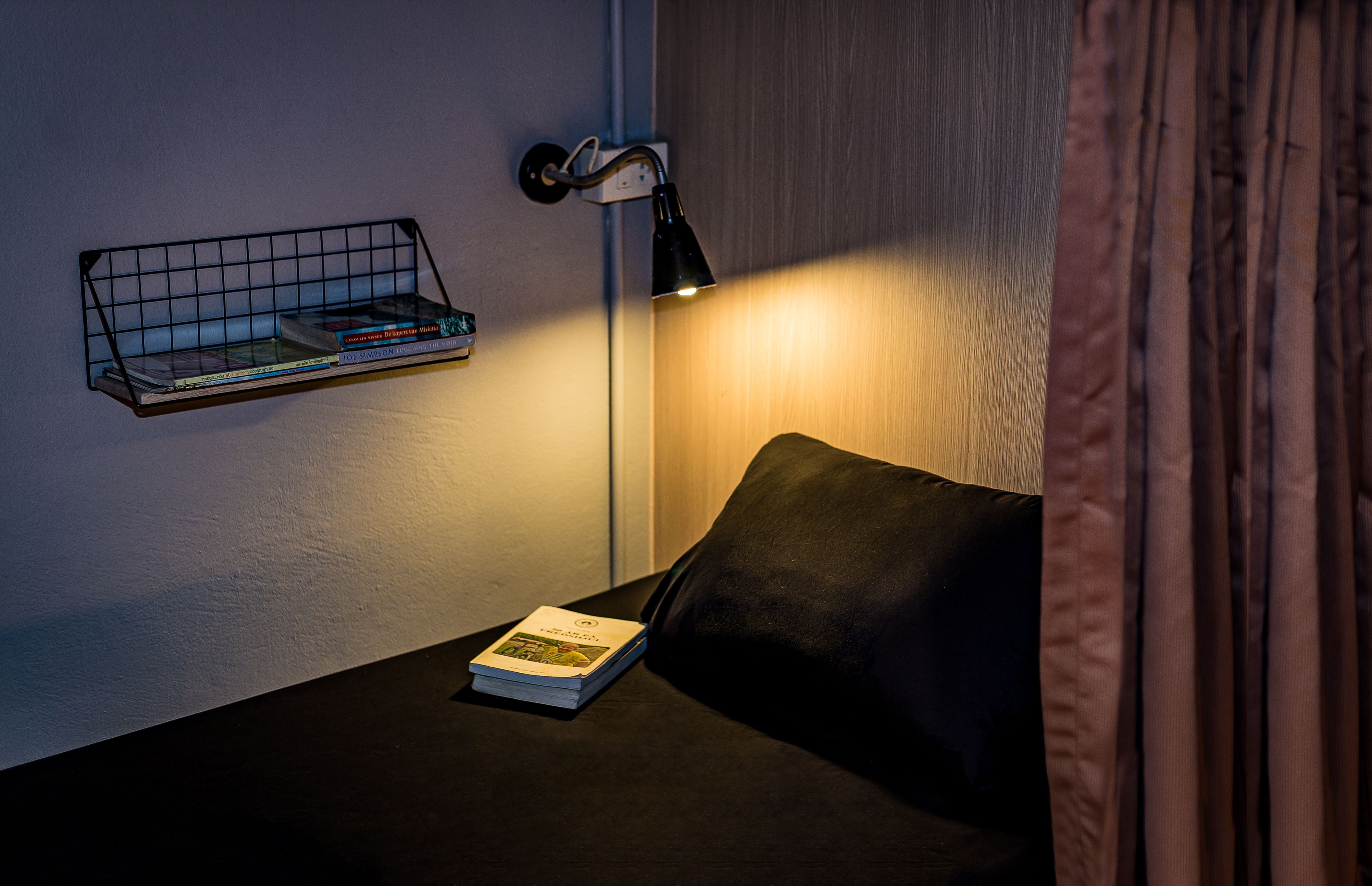A neatly arranged reading area with a black sofa, a small side table, a wall-mounted book rack, and a floor lamp.