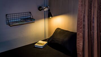 A neatly arranged reading area with a black sofa, a small side table, a wall-mounted book rack, and a floor lamp.