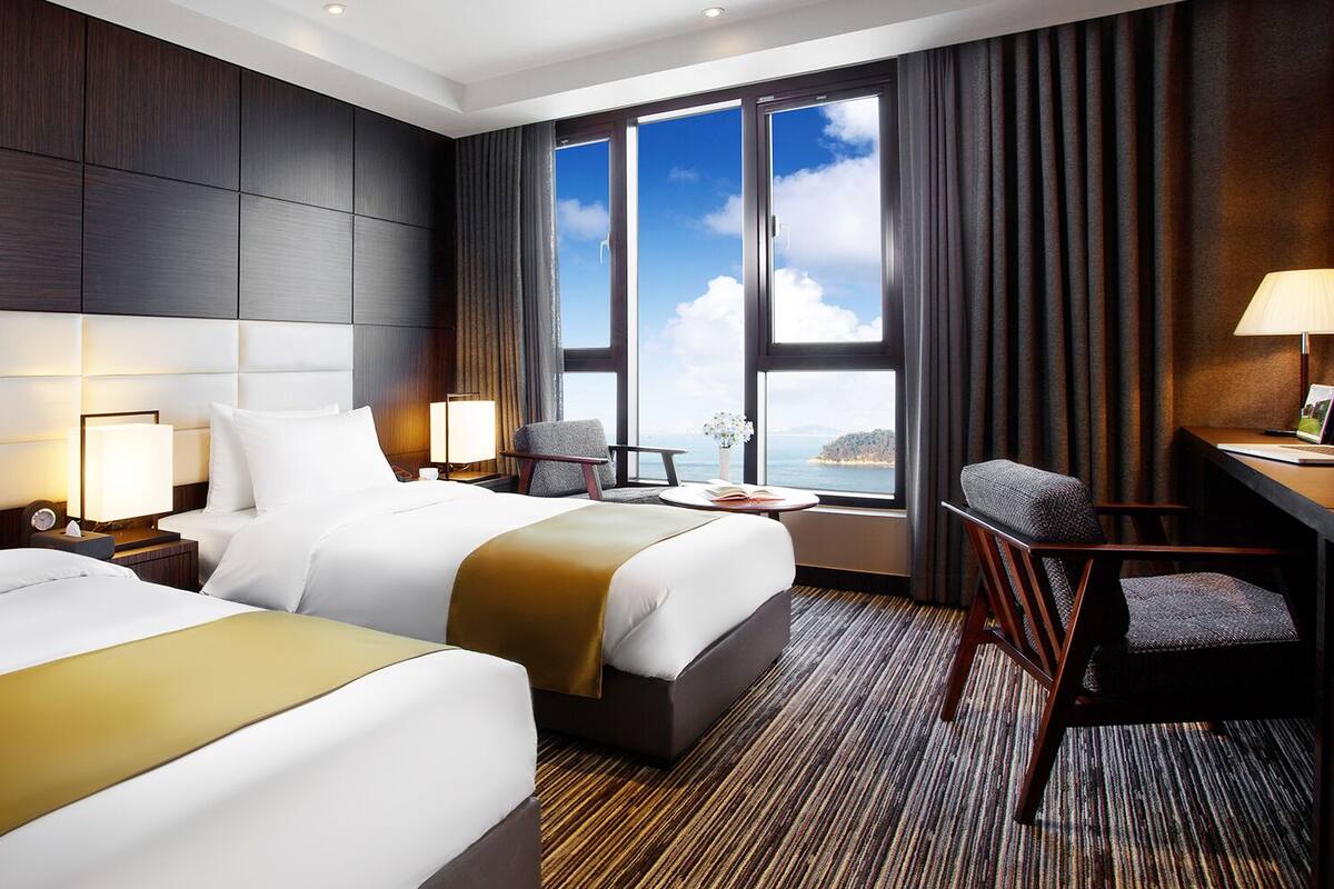 Habitación de hotel con dos camas, un escritorio, una silla y vista al mar.