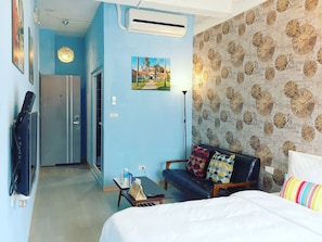 Une chambre d’hôtel avec un lit, un canapé, un bureau avec une lampe, un tableau au mur et un papier peint à motifs d’horloges.