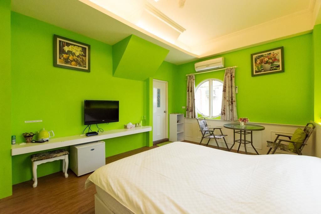 A room with a bed, a desk with a TV, a small fridge, and a window with curtains.