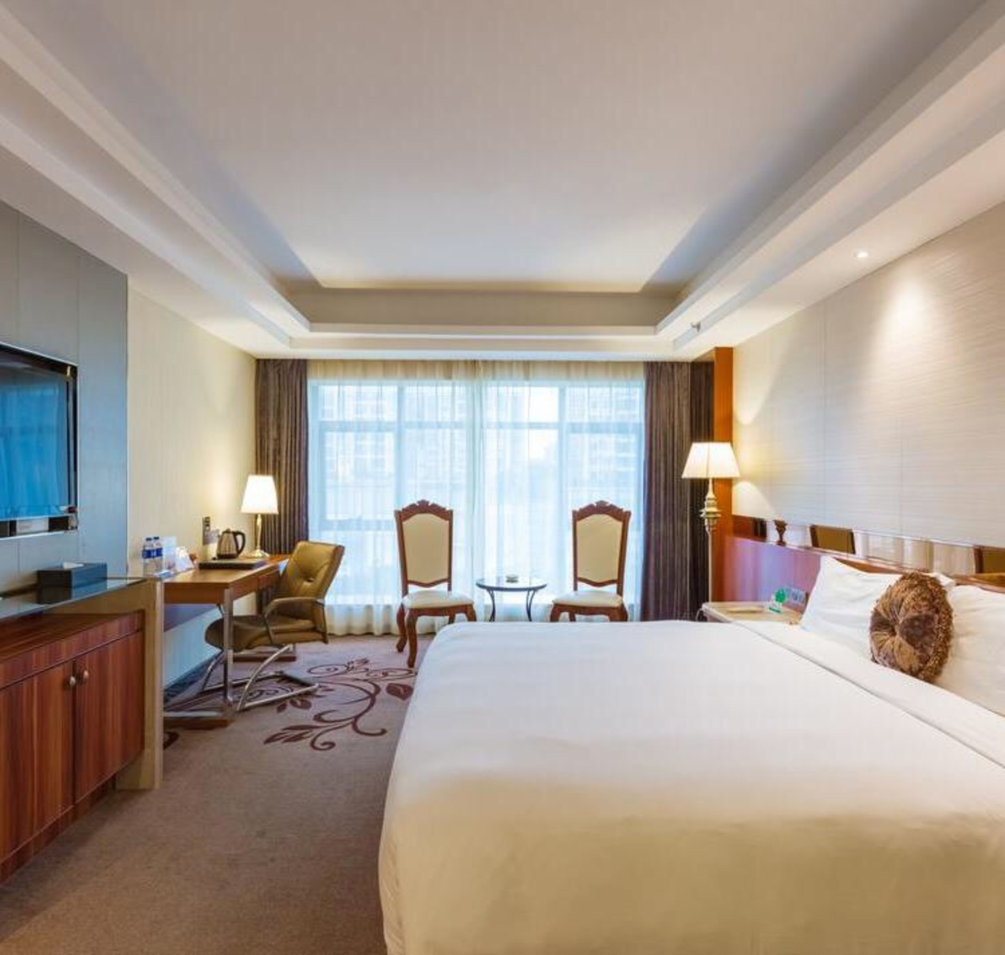 A hotel room with a large bed, a desk with a chair, two chairs, a TV, and a window with curtains.