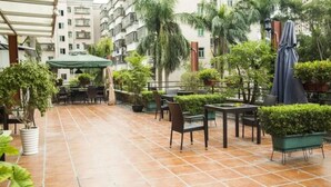 An outdoor patio area with tiled flooring, multiple tables and chairs, potted plants, and a covered seating area. - Zhuhai Asian Star Hotel (Zhuhai)