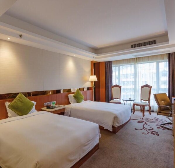 A hotel room with two beds, a desk, a chair, and a large window.