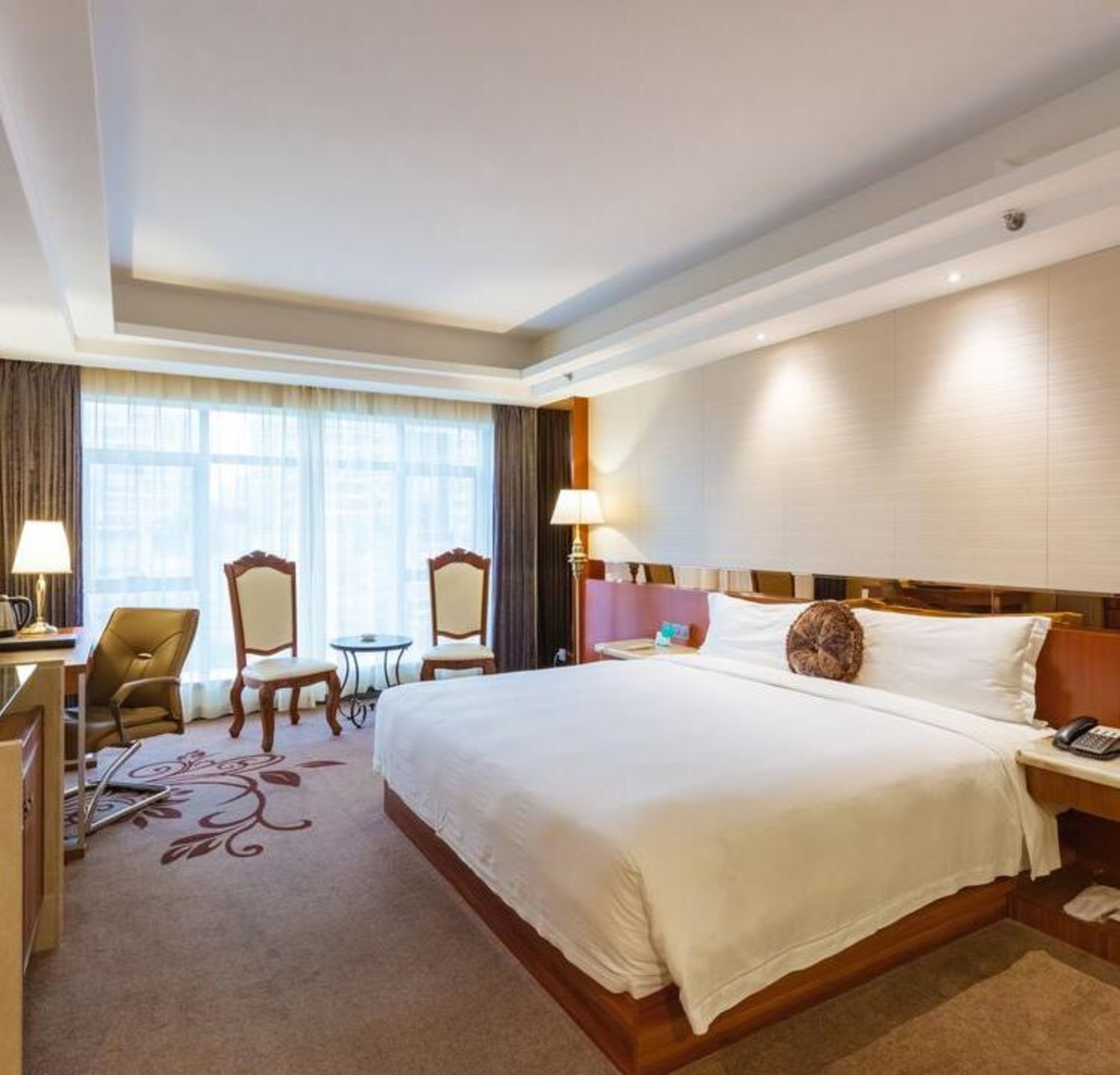 Une chambre d’hôtel avec un grand lit, deux chaises, un bureau et une lampe.