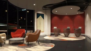 Un hall d’entrée moderne doté d’un espace salon comprenant un fauteuil rouge et un fauteuil beige, une grande fenêtre donnant sur un pont, et trois vases décoratifs disposés sur une plateforme circulaire.