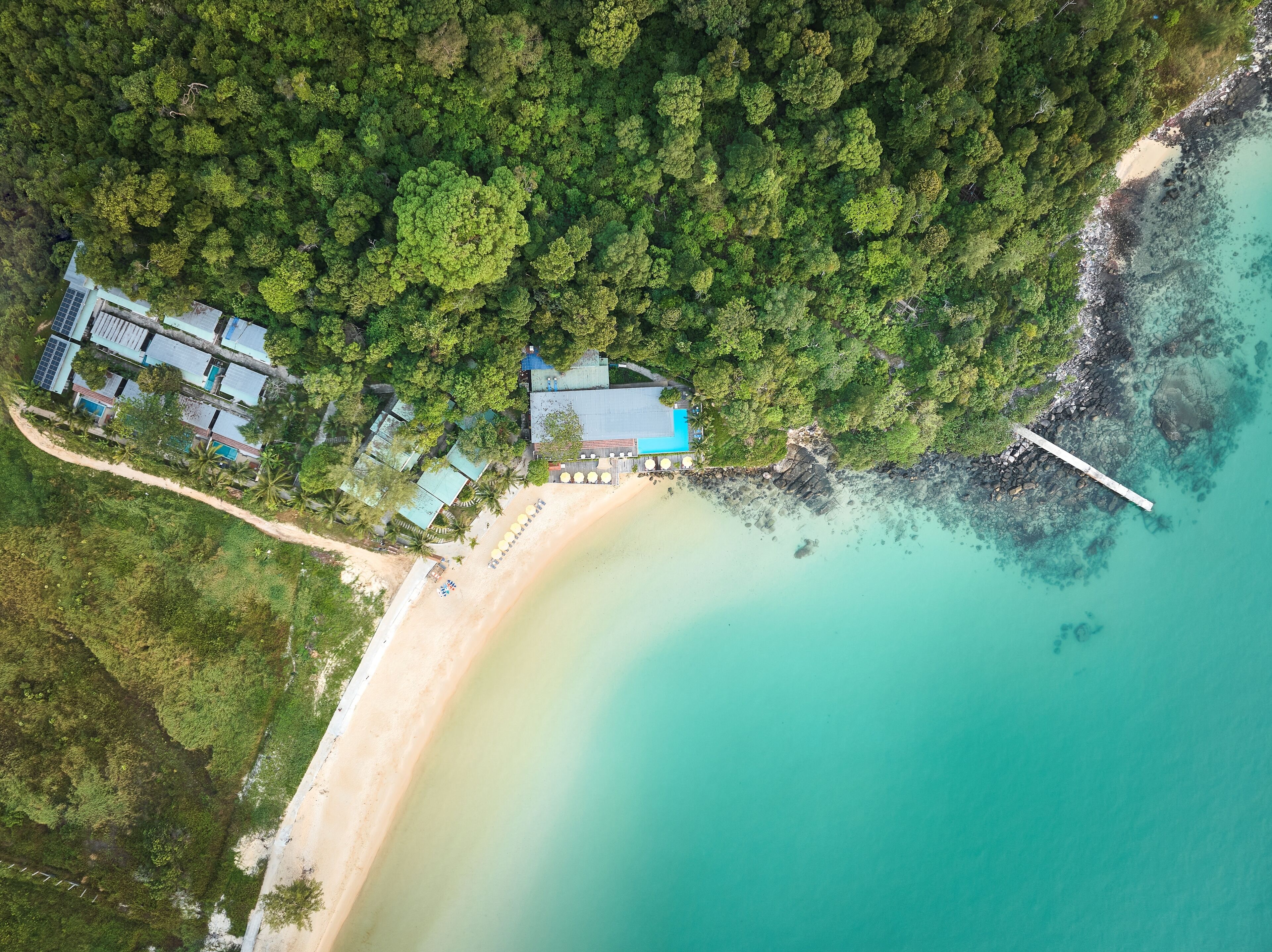 Vista aérea de una propiedad costera con playa, muelle y un grupo de edificios.