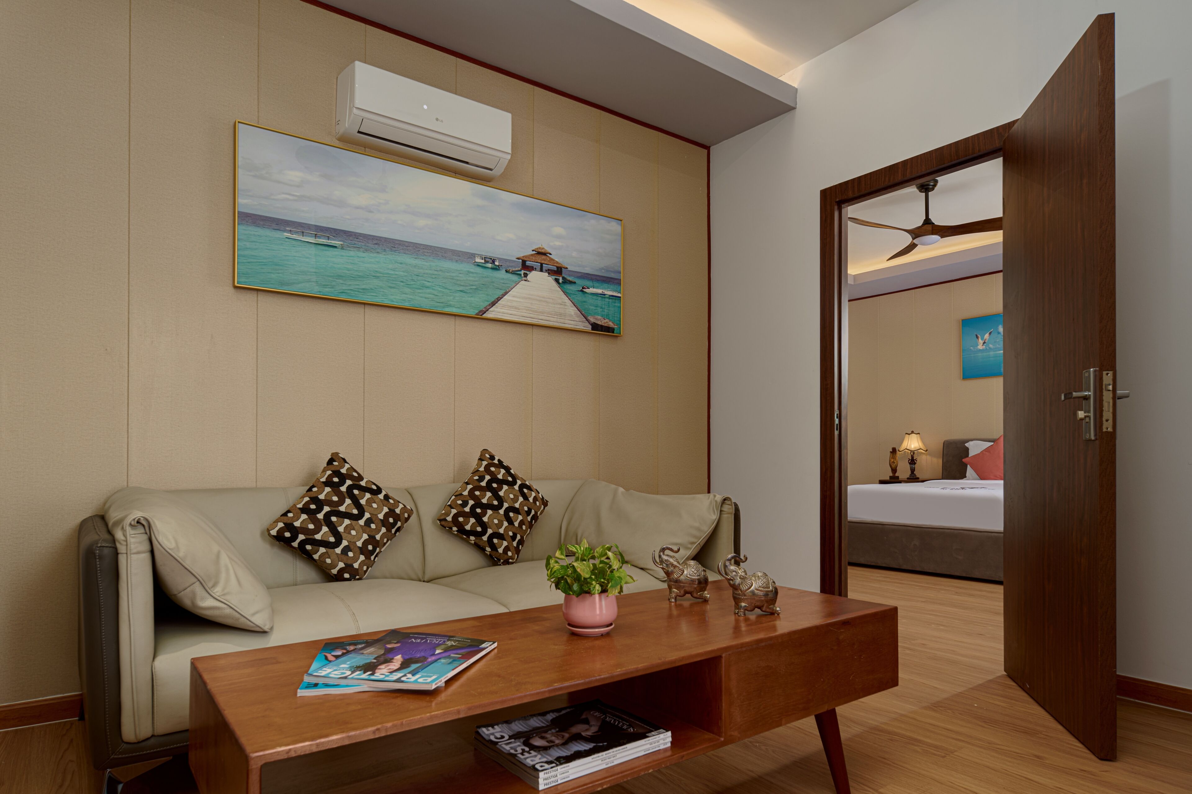 Een kamer met een bank, een salontafel met tijdschriften, een schilderij van een pier, een airconditioner en een bed met nachtkastje.