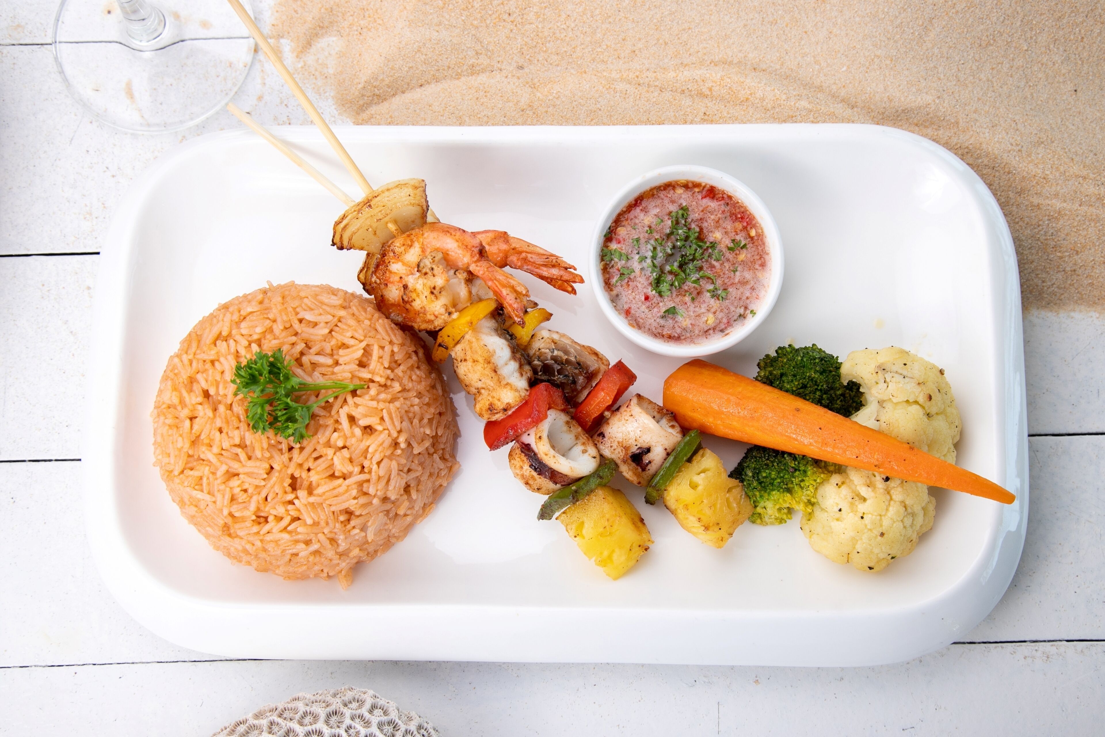 A white rectangular plate with rice, shrimp, vegetables, and a sauce.