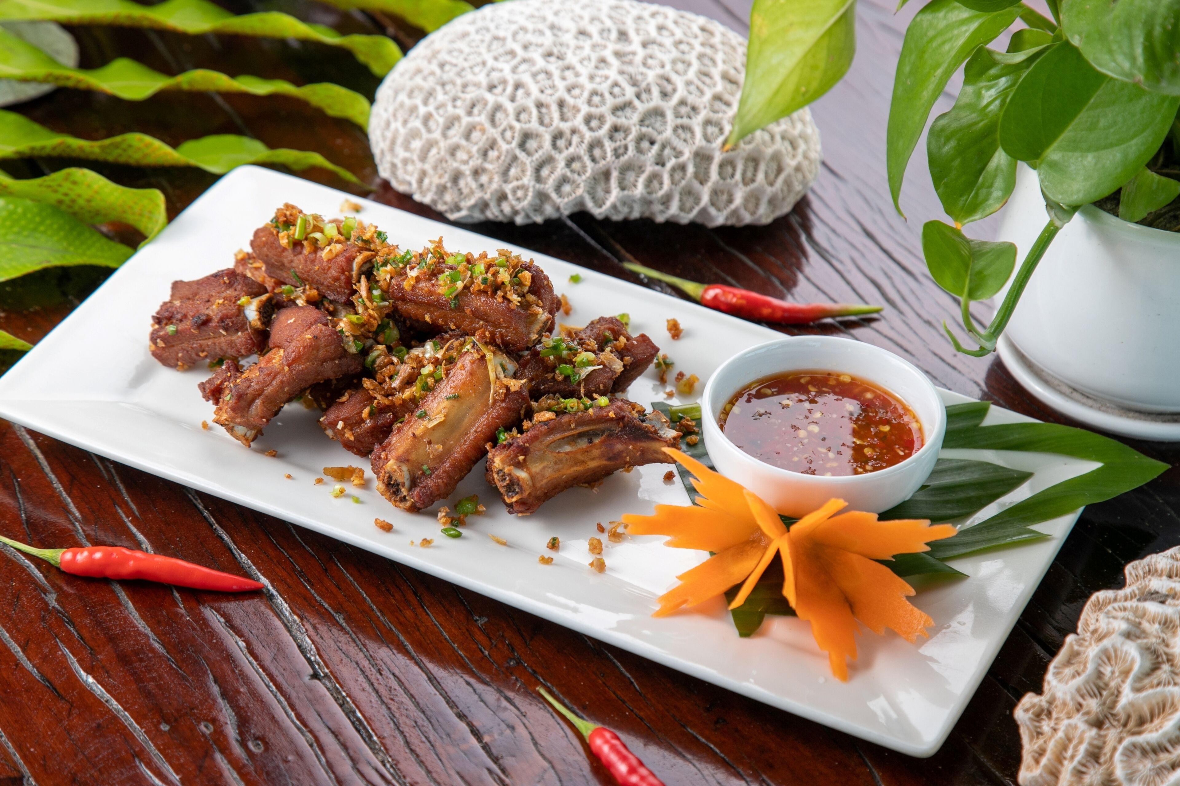 A plate of grilled meat with a side of dipping sauce and garnishes, set on a wooden table with decorative elements.