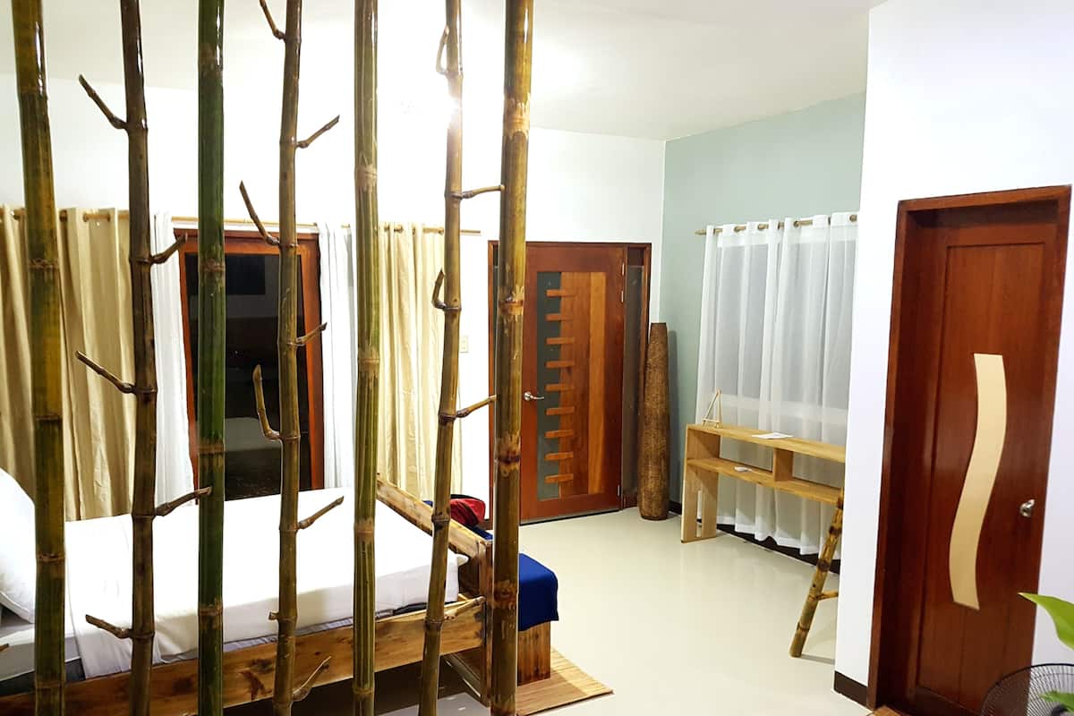 A room with a bed, a wooden bench, a door, and a window with curtains.