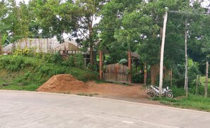 A rural road with a dirt path leading to a wooden structure with a thatched roof.