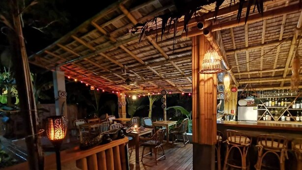 An outdoor bar area with wooden furniture, string lights, and a bamboo ceiling. - La Colonial Resort - Adults Only (El Nido)