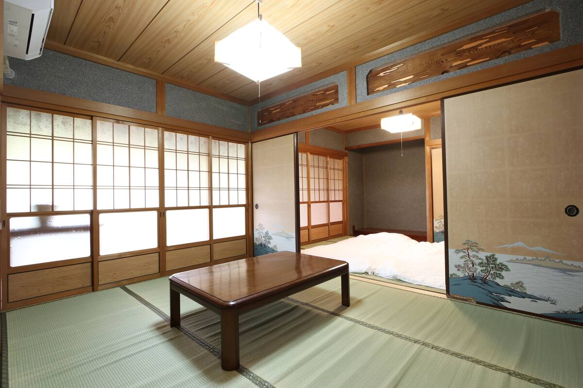 A traditional Japanese room with tatami flooring, a low wooden table, sliding doors, and a view of a snowy landscape through a paper screen.