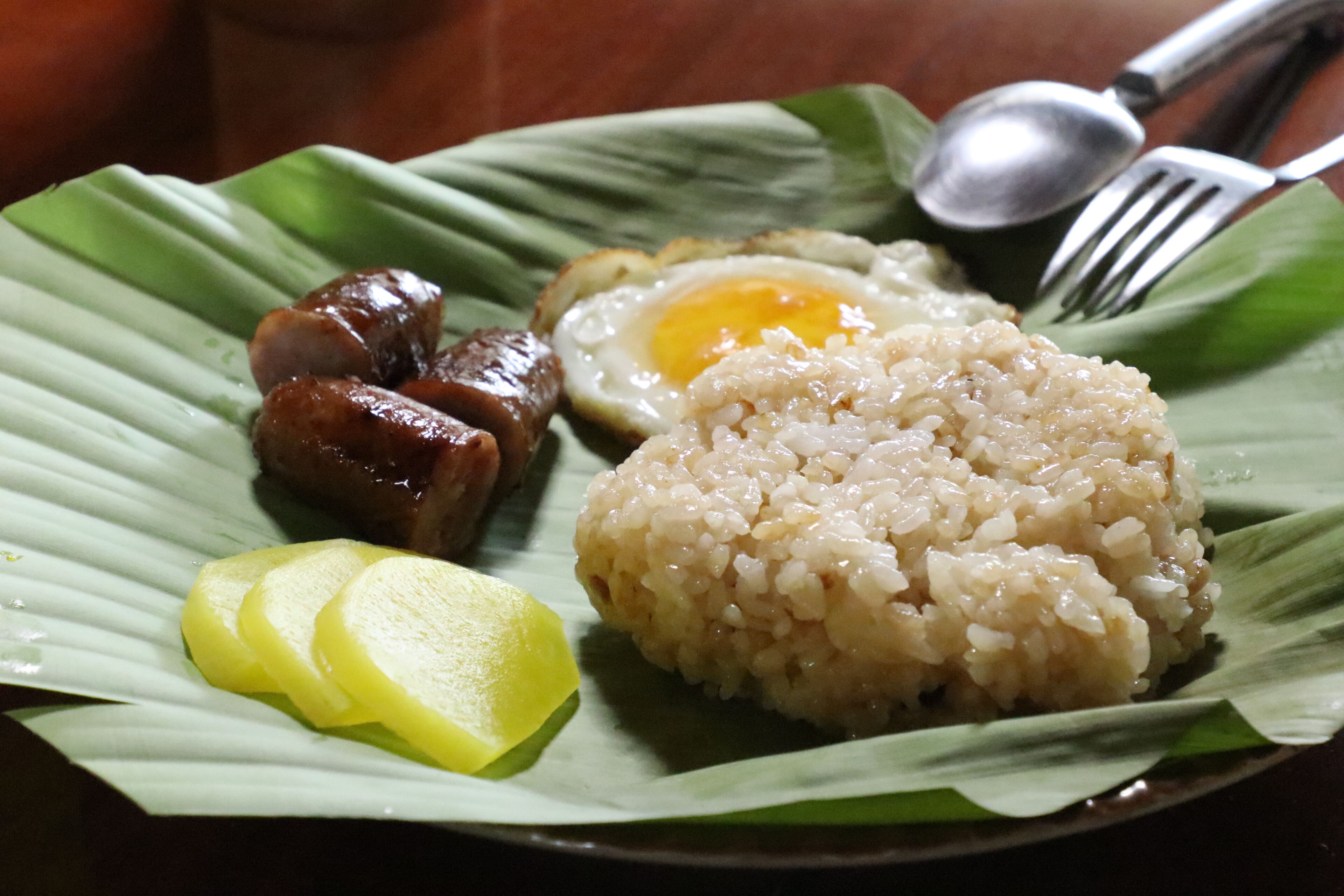 A plate of food with rice, a fried egg, and sausages on a banana leaf.