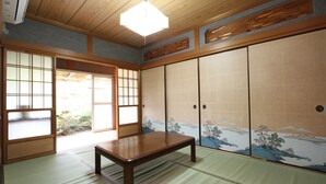 Una habitación japonesa tradicional con suelo de tatami, una mesa baja de madera, puertas correderas shoji y vistas a un paisaje montañoso.