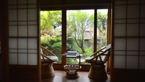 Una habitación japonesa tradicional con suelo de tatami, una puerta corredera que da a un jardín y dos sillas de madera.