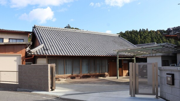 Una casa japonesa tradicional con tejado de tejas, una puerta de madera y un camino de hormigón.