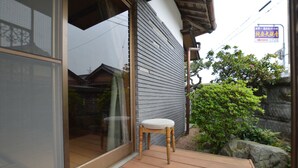 Una terraza de madera con una silla, un ventanal corredero y un muro de piedra con vegetación.