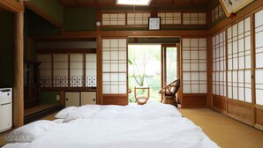 Una habitación japonesa tradicional con suelo de tatami, futón, puertas correderas y vistas a un jardín.