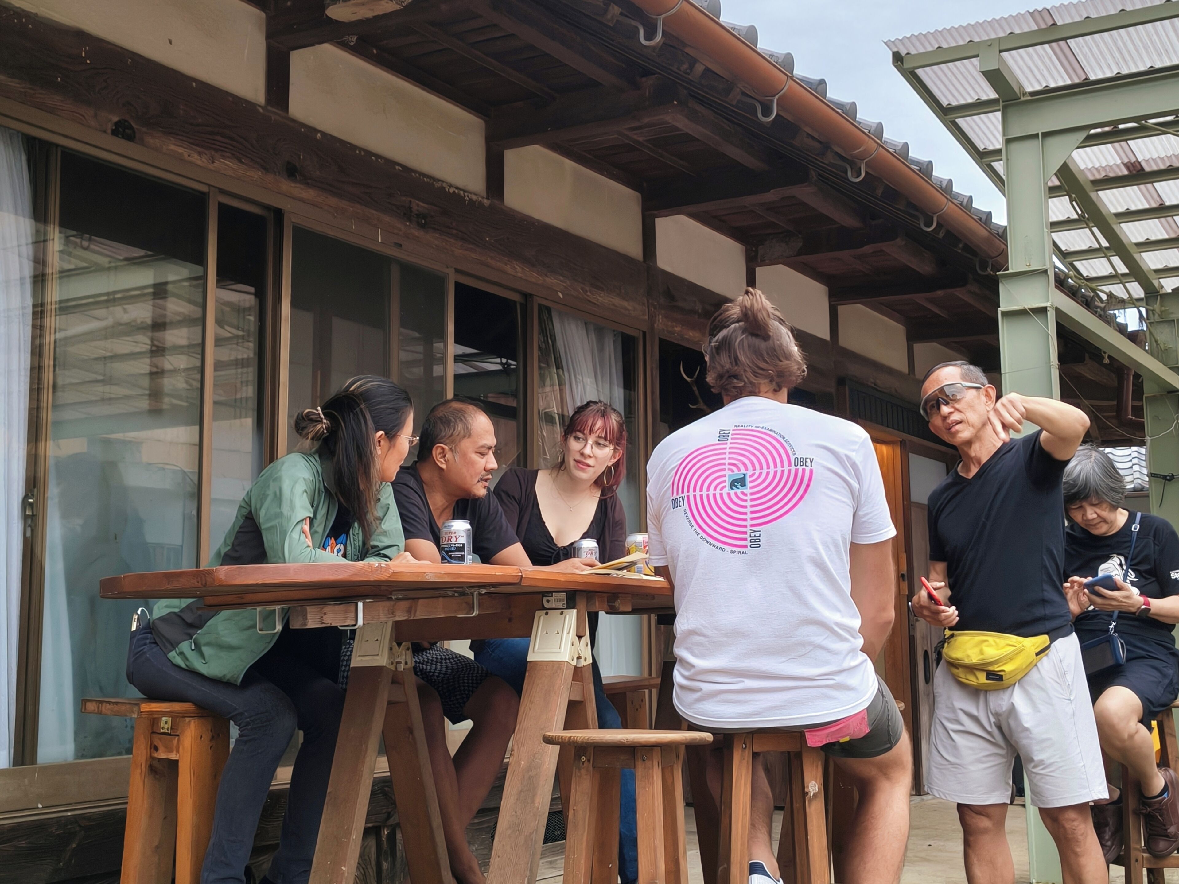 Un grupo de personas sentadas en una mesa de madera al aire libre, con un edificio tradicional de fondo.
