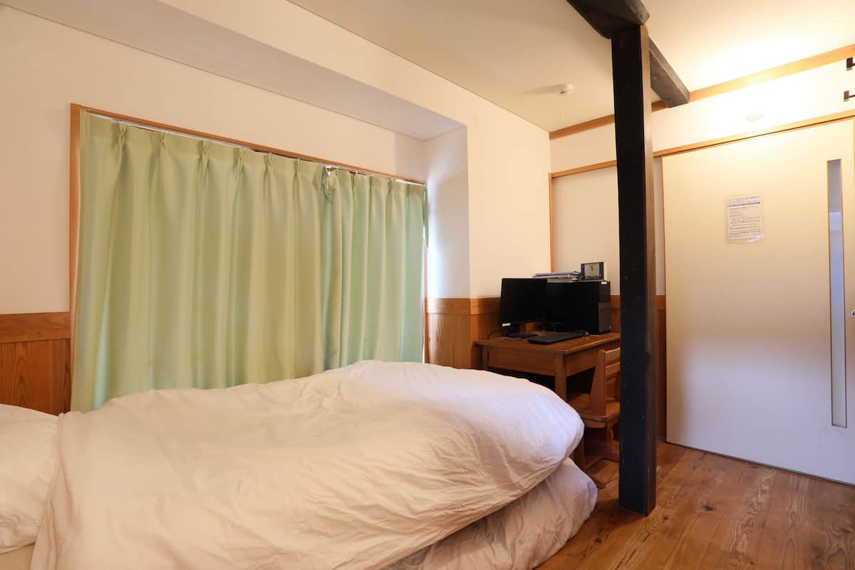 A hotel room with a bed, a desk with a television, and a wooden floor.
