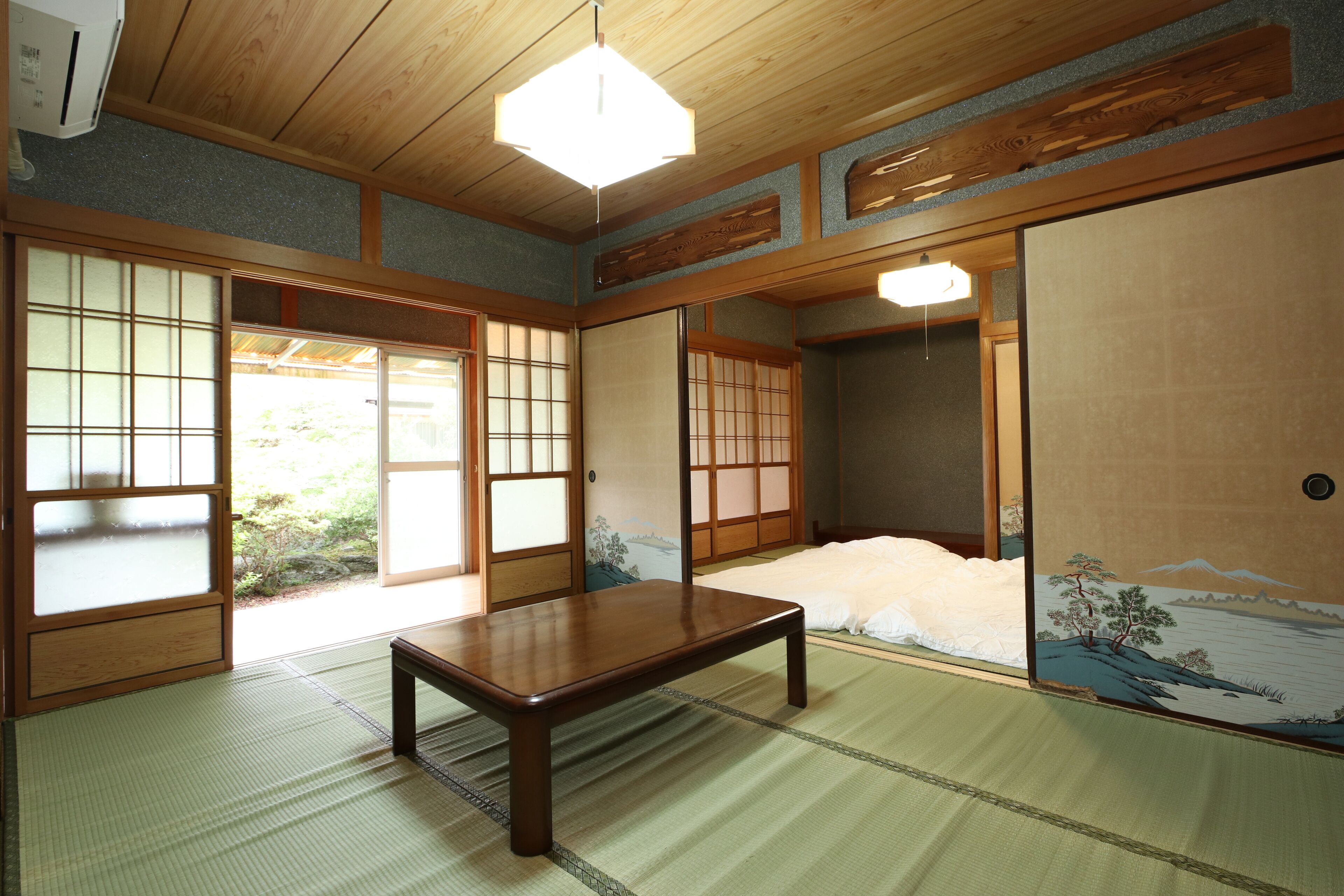 Una habitación japonesa tradicional con suelo de tatami, una mesa de madera baja, puertas correderas y vistas a un paisaje montañoso.