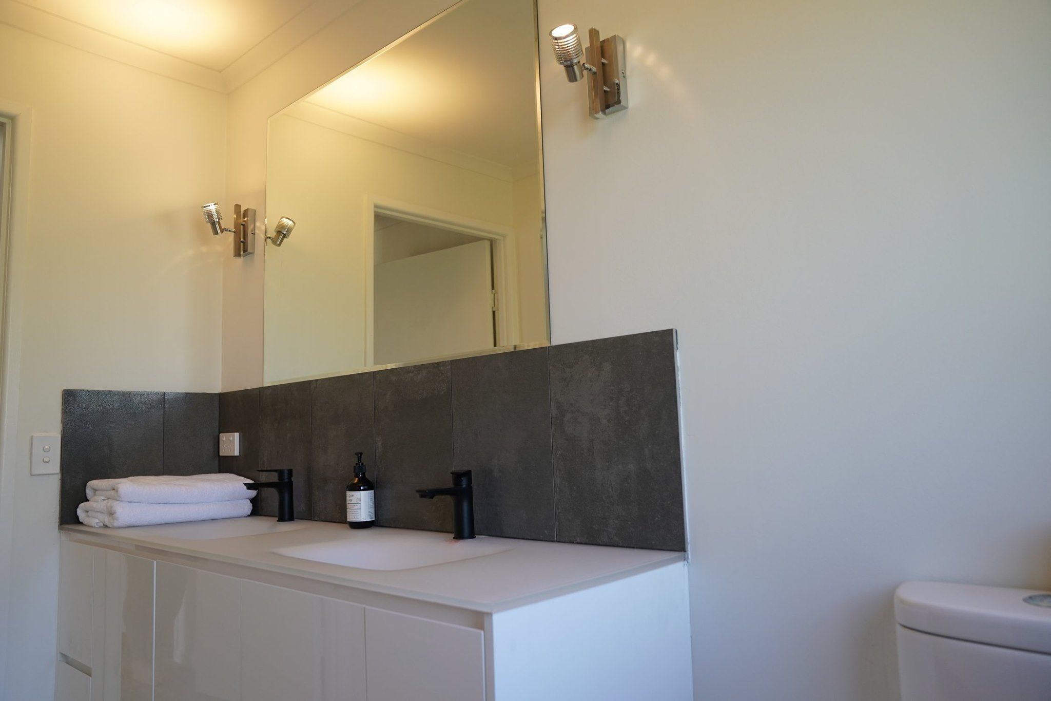 A bathroom with a large mirror, a white sink, a black faucet, and a toilet.
