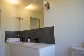 Un baño con un espejo grande, un lavamanos blanco, un grifo negro y un inodoro.