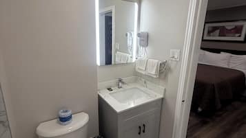 Un baño con inodoro, lavamanos, espejo y cubo de basura.