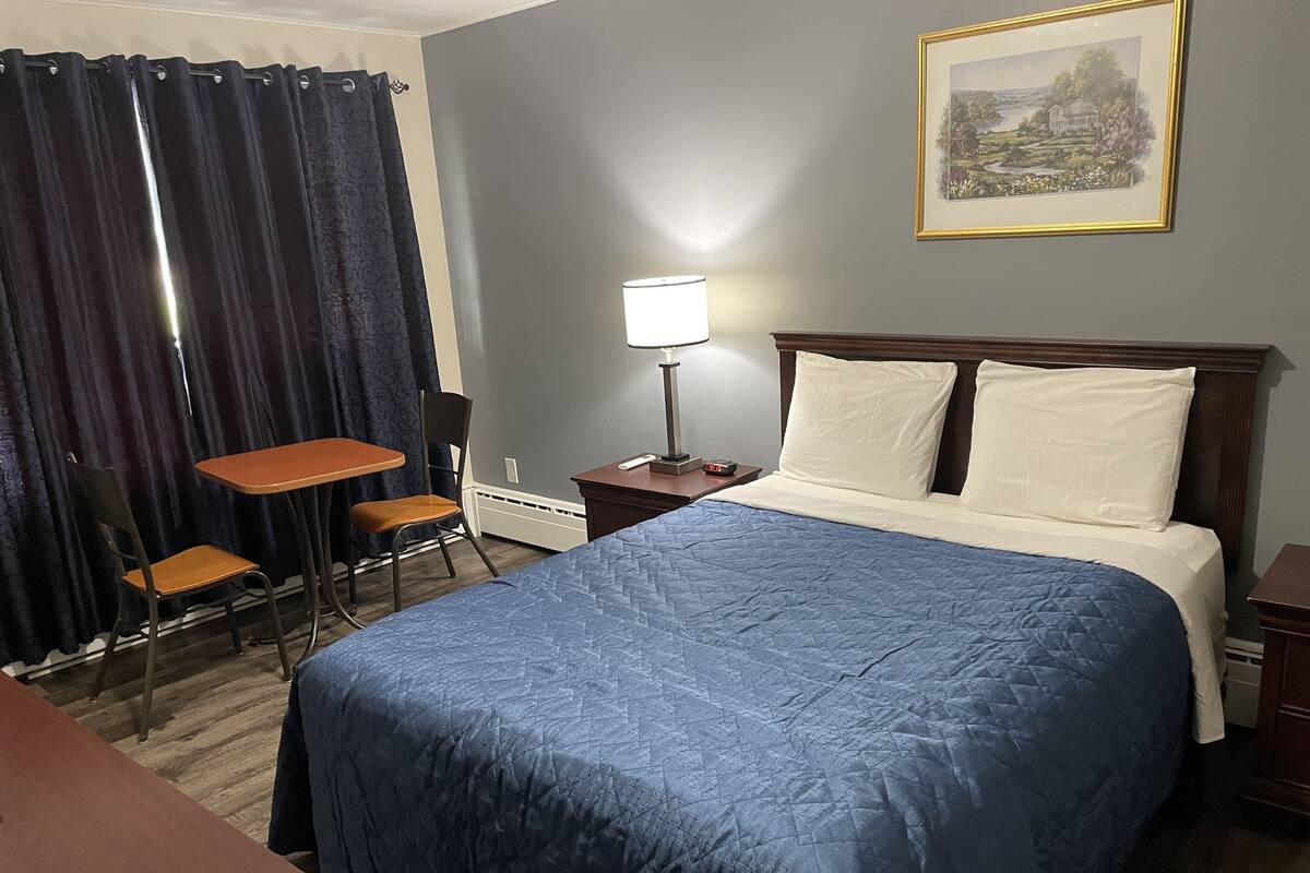Habitación de hotel con cama, escritorio, silla, lámpara y un cuadro en la pared.