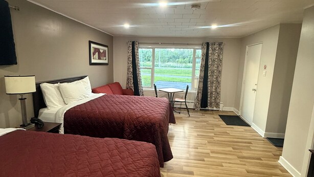 A hotel room with two beds, a desk, a chair, a window with curtains, and a door. - Nites Inn Motel (Cornwall)