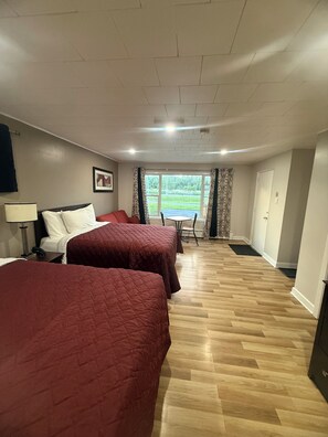 A hotel room with two beds, a desk, a chair, a window with curtains, and a door.