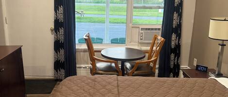 Una habitación de hotel con cama, una mesa con sillas, una lámpara y una ventana con cortinas.