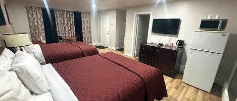 Habitación de hotel con dos camas, televisión, refrigerador, escritorio y silla.