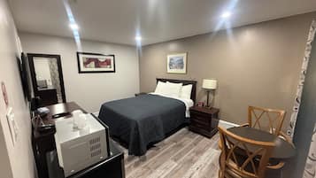 A hotel room with a bed, a desk with a computer, a chair, and a small table.