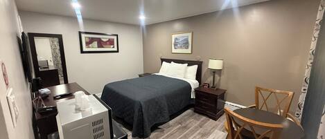 A hotel room with a bed, a desk with a computer, a chair, and a small table.