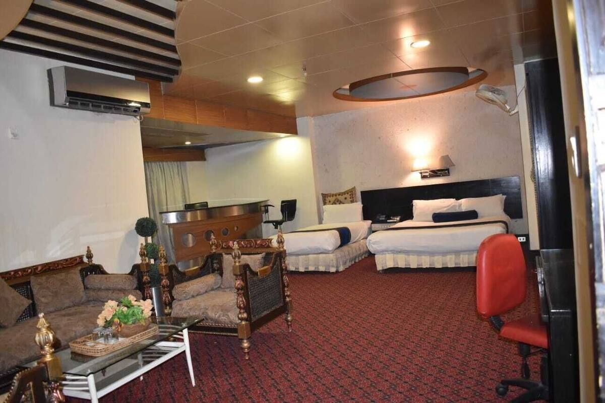 A hotel room with two beds, a sofa, a dining table, and a red chair.