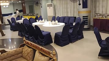A banquet hall with round tables, blue-covered chairs, and a central chandelier.