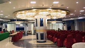 Un amplio salón con filas de sillas rojas, una columna central e iluminación empotrada en el techo.